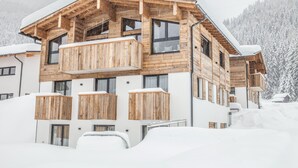 Una cabaña de madera de varios pisos con balcones, ubicada en una zona montañosa nevada.