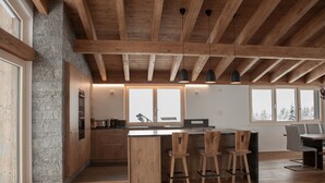 Una cocina moderna con vigas de madera, un muro decorativo de piedra y una isla grande con taburetes de bar.