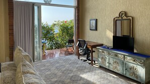 A bedroom with a large window, a desk, a chair, a bed, and a dresser.