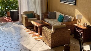 A sunlit living room with a view of the sea, featuring wicker furniture, a coffee table, and a floor lamp.