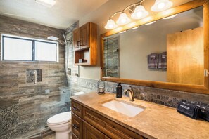 A bathroom with a large mirror, a sink, a toilet, and a shower area.