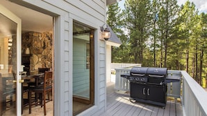 A deck with a barbecue grill, a dining table with chairs, and a stone wall visible through a glass door. - Newly Updated Mtn House! Walk to Golf/Tennis/Park, Hot Tub, Firepit, Ping Pong (Angel Fire)