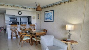 A living room with a sofa, a dining table with chairs, a kitchen area with a microwave, and a lamp.