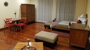 Habitación de hotel con mesa de comedor de madera, sillas, sofá, cama, mesita de noche, lámpara y armario.