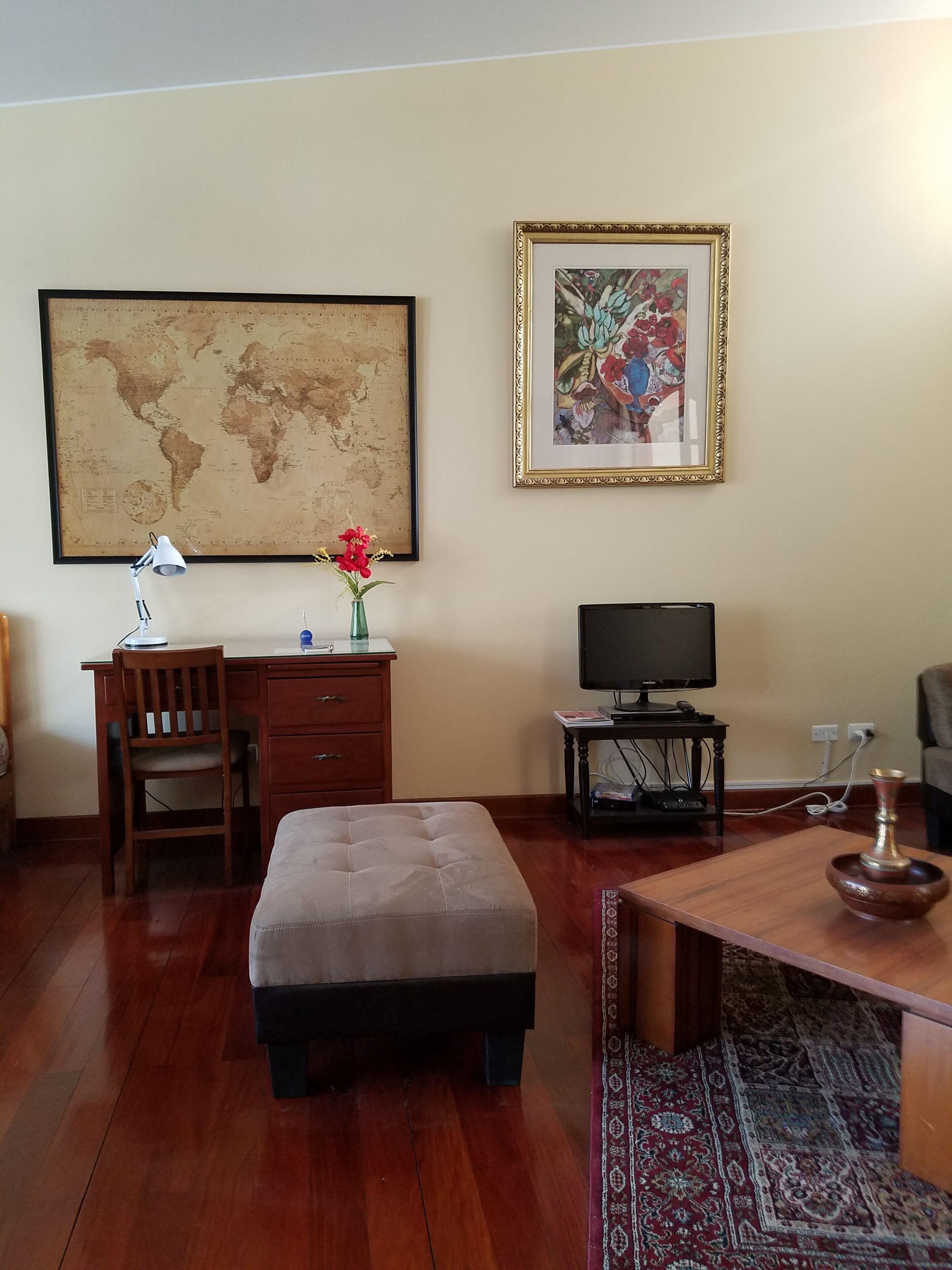 A living room with a wooden desk, a television, a large world map, and a framed painting.