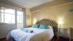 A hotel room with a large bed, two bedside lamps, a nightstand, and a window with curtains.