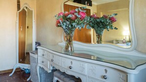 A white dresser with a mirror, two vases with flowers, and a wicker basket.
