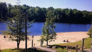 A lakeside view with a sandy beach, a wooden deck, and a grassy area.