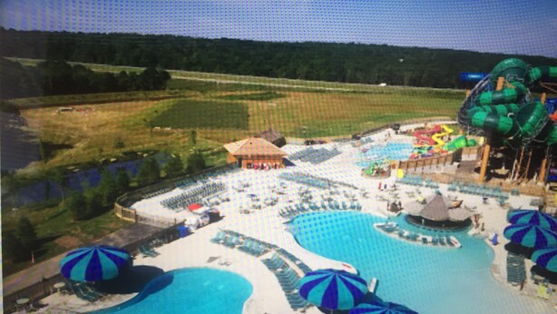 A water park with multiple pools, umbrellas, and a large slide.