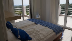Un dormitorio con cama, mesita de noche y ventana con vista a un balcón y follaje.
