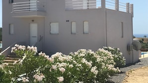 Un edificio de dos pisos con balcón, una puerta y ventanas con contraventanas.