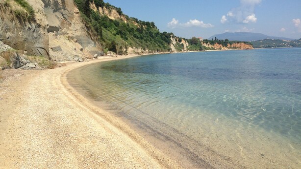 Una playa costera con aguas cristalinas, arena dorada y un acantilado rocoso.