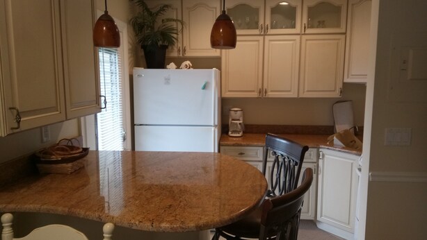 A kitchen with a granite countertop, white cabinets, a refrigerator, a coffee maker, and a potted plant.
