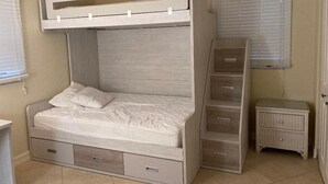 A bunk bed with a ceiling fan, a bedside table, and a nightstand.