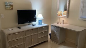 A room with a TV on a cabinet, a lamp, a mirror, and a painting on the wall.