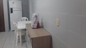 Une petite cuisine équipée avec un réfrigérateur blanc, une table et deux chaises blanches.