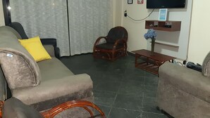Un salon comprenant un canapé, deux fauteuils, une table basse en bois, un téléviseur fixé au mur et une fenêtre avec des rideaux.