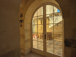 A stone doorway with a large arched window leading to an outdoor patio with stone flooring and wooden furniture. - Large modern farmhouse with private pool & BBQ, stunning views, perfect location (Ir-Rabat Għawdex)