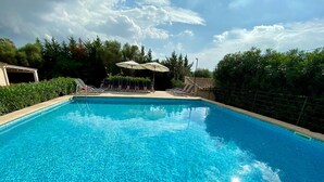 Une piscine rectangulaire à l’eau d’un bleu cristallin, entourée d’une haie basse et agrémentée de quelques chaises longues placées sous des parasols.