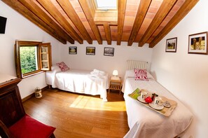 Une chambre avec deux lits, des poutres en bois au plafond, une fenêtre avec vue et des tableaux encadrés au mur.