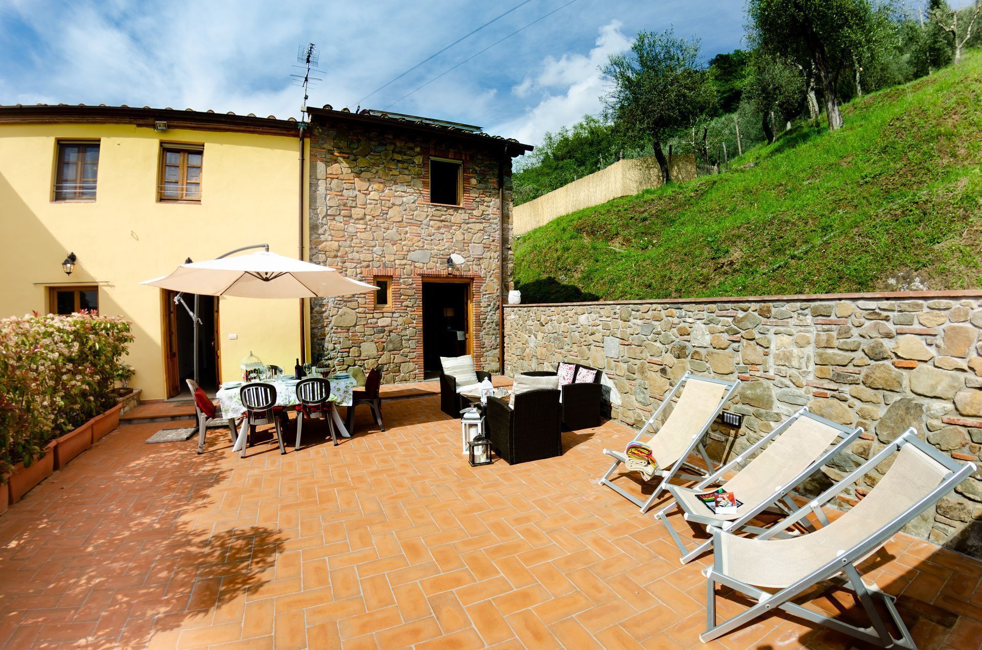 A patio with a table and chairs, a stone wall, and a building with a yellow facade.