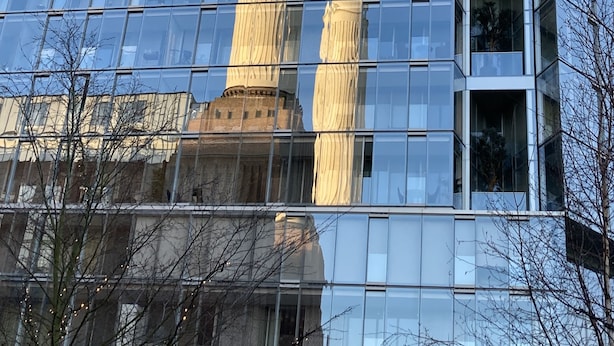 A modern building with reflective glass windows and a prominent cylindrical structure in the background.