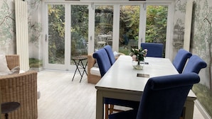 A conservatory with a dining table, blue chairs, a wicker chair, and a vase of flowers.
