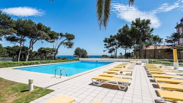 A pool area with sun loungers and a clear view of the sea.