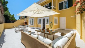A yellow building with a patio area featuring wicker furniture, a table with plates and glasses, and a large umbrella.