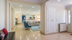 A spacious living area with a sofa, chairs, and a dining table. There is a white door and a radiator on the wall.