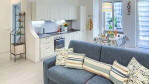 A modern kitchen with white cabinets, a dining area with a table and chairs, and a grey sofa with striped cushions. - Casa Mary - For 4 people, in centre, 5 minutes from beach and station to Cinque Terre (Levanto)
