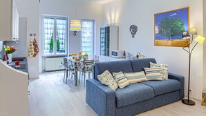 A modern living room with a blue sofa, dining table, and kitchen area in the background. - Casa Mary - For 4 people, in centre, 5 minutes from beach and station to Cinque Terre (Levanto)