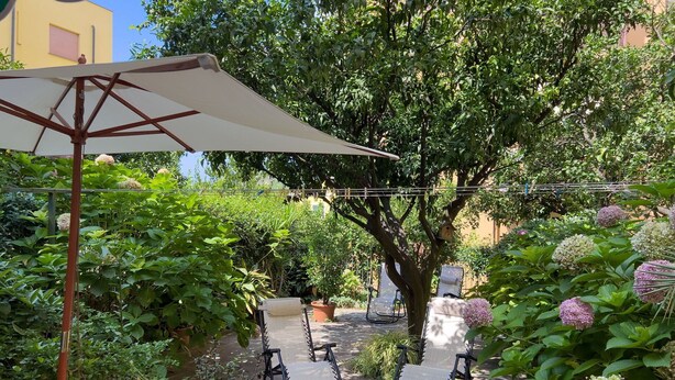 An outdoor seating area with two lounge chairs and a large umbrella, surrounded by lush greenery and flowering plants. - Casa Mary - For 4 people, in centre, 5 minutes from beach and station to Cinque Terre (Levanto)