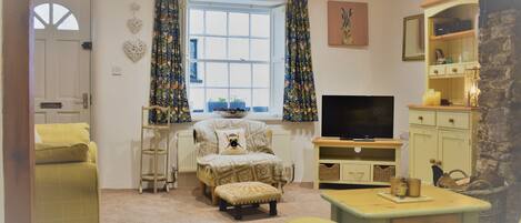 A cozy living room with a sofa, ottoman, and a television.