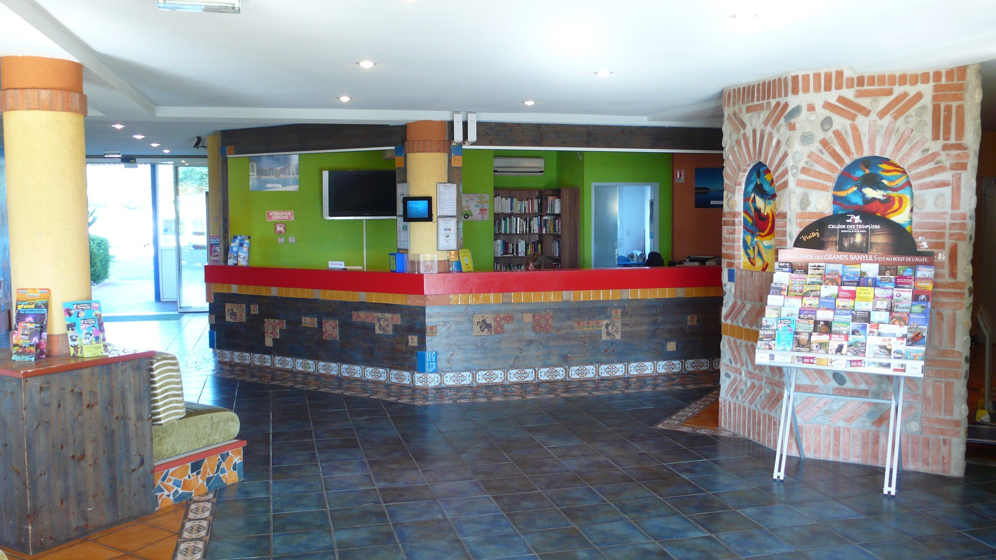 Un área de recepción con piso de baldosas, mostrador de cubierta roja y pared con diseño de mosaico.