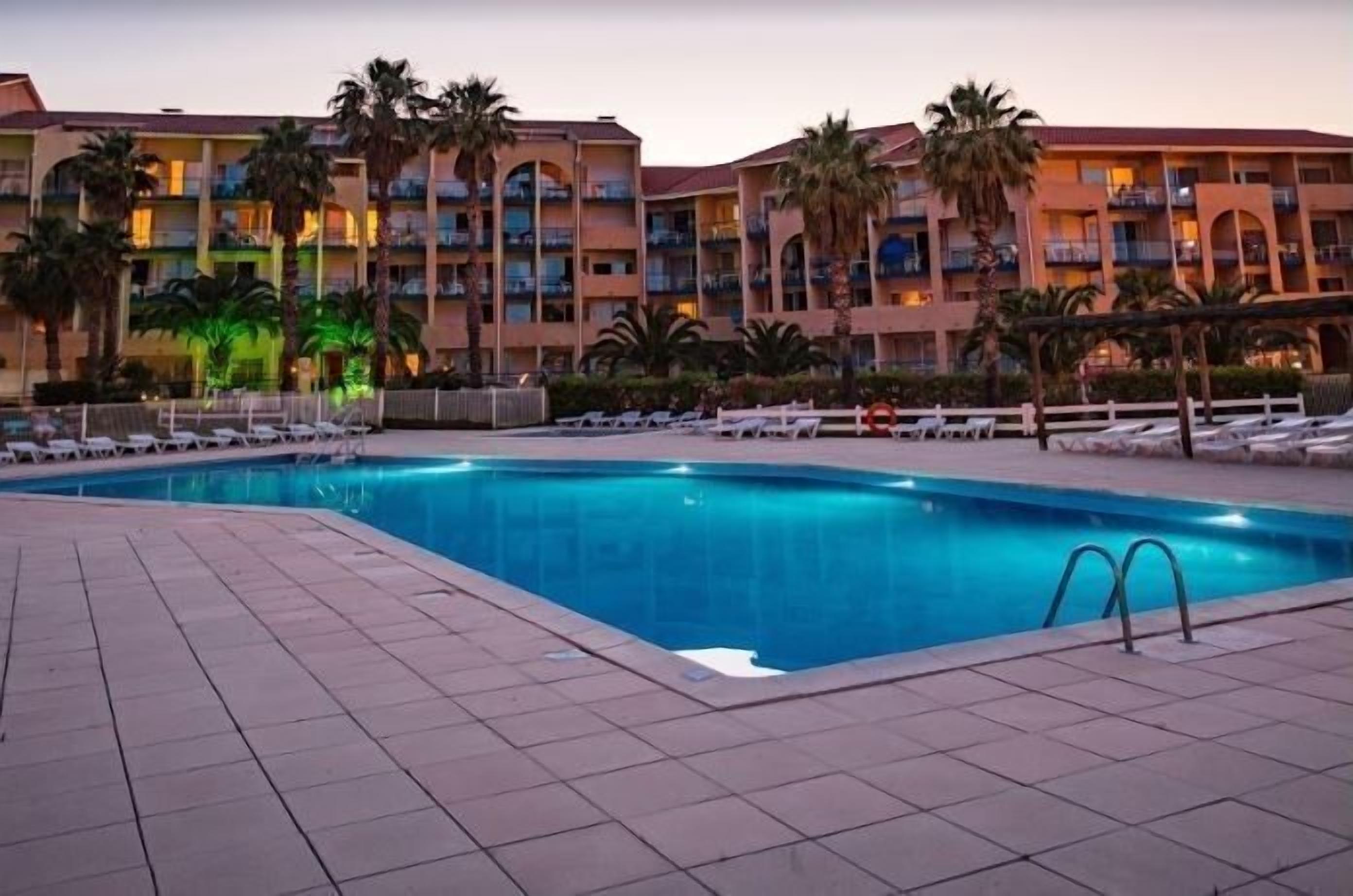 Zona de piscina de hotel con una piscina azul cristalina, sillas de descanso y palmeras.