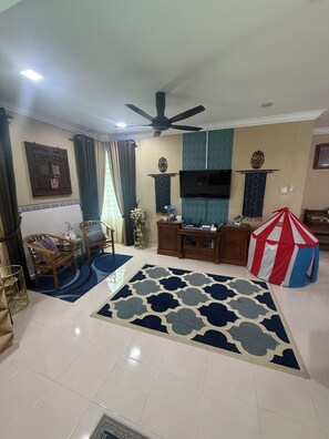 A living room with a flat-screen TV, a ceiling fan, a wooden cabinet, and a red and white striped play tent. - RizQin Homestay Bachok (Bachok)