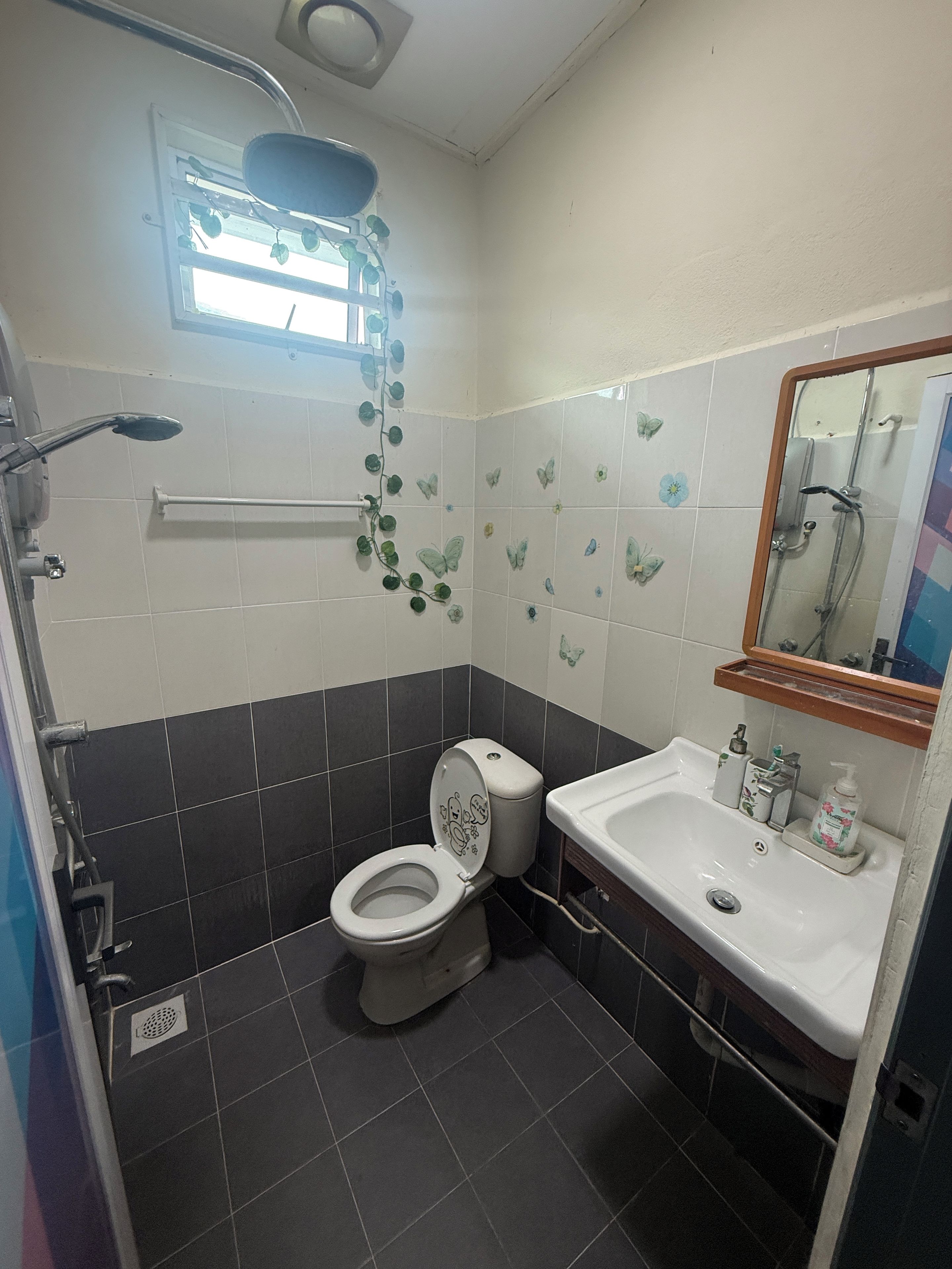 A bathroom with a toilet, sink, shower, and a window with a view.