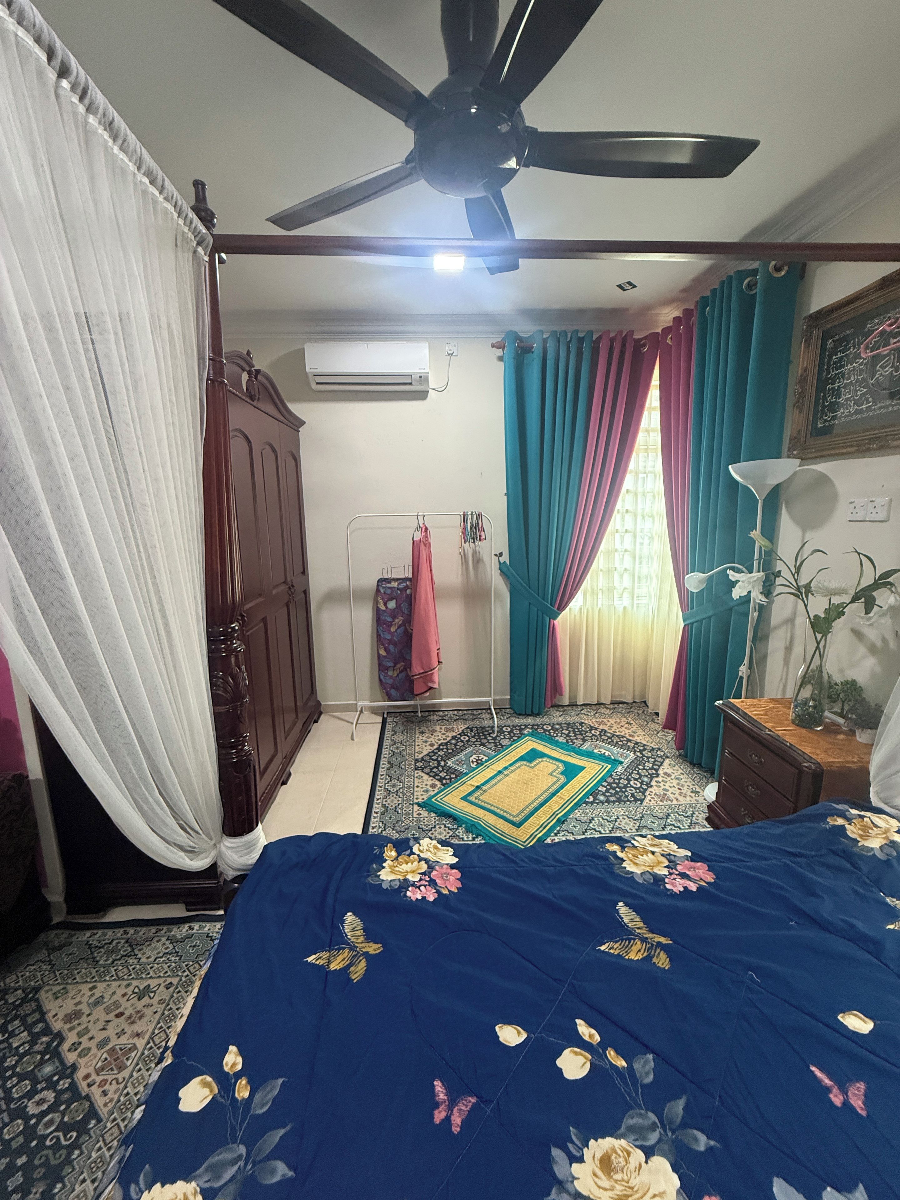 A bedroom with a bed, a ceiling fan, a window with curtains, an air conditioning unit, and a wall-mounted lamp.