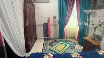 A bedroom with a bed, a ceiling fan, a window with curtains, an air conditioning unit, and a wall-mounted lamp.