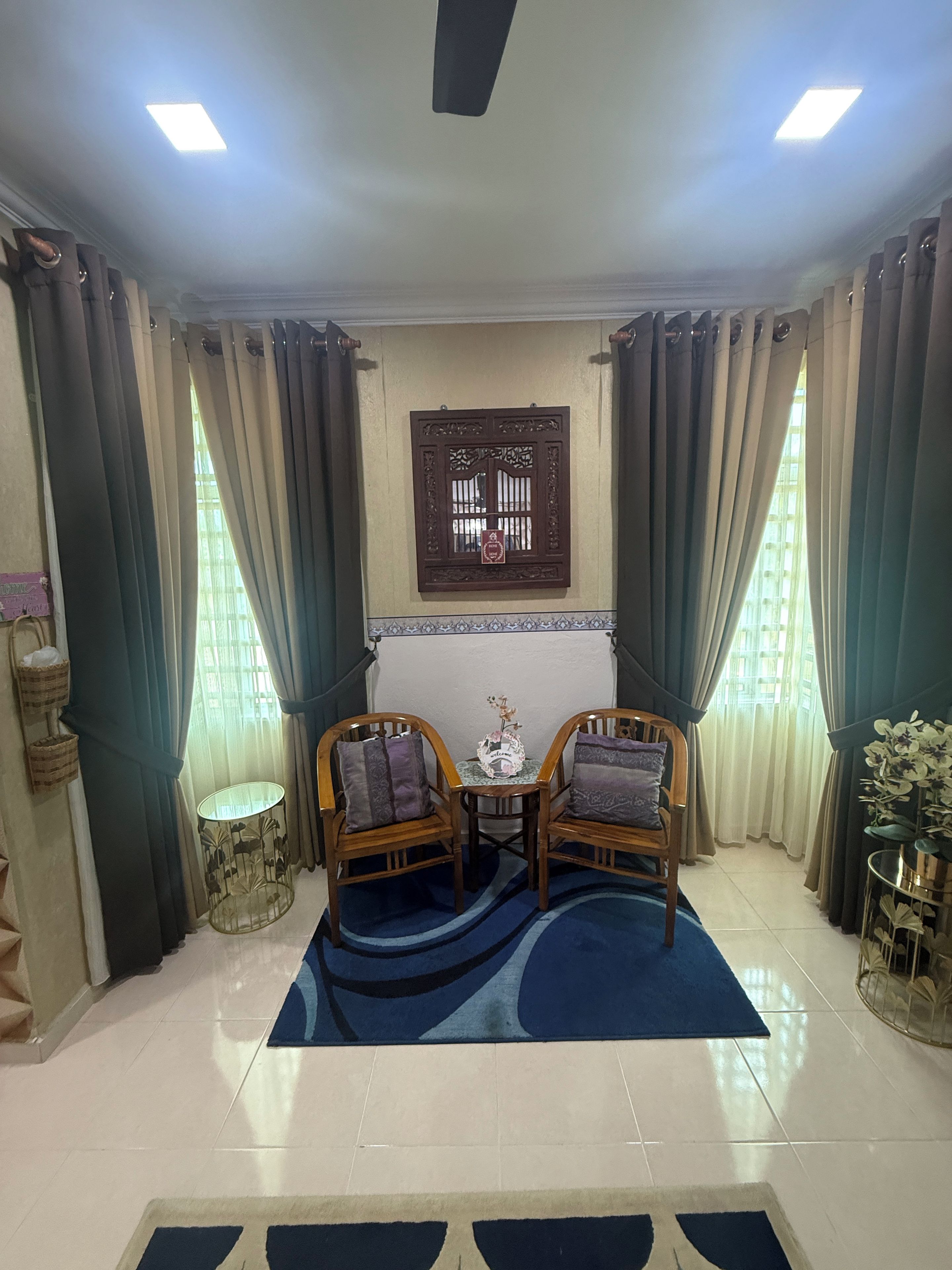 A room with two wooden chairs, a small table, a decorative wall piece, and a blue rug.