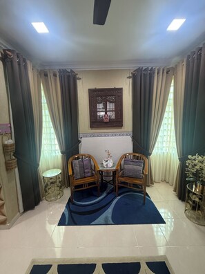 A room with two wooden chairs, a small table, a decorative wall piece, and a blue rug. - RizQin Homestay Bachok (Bachok)