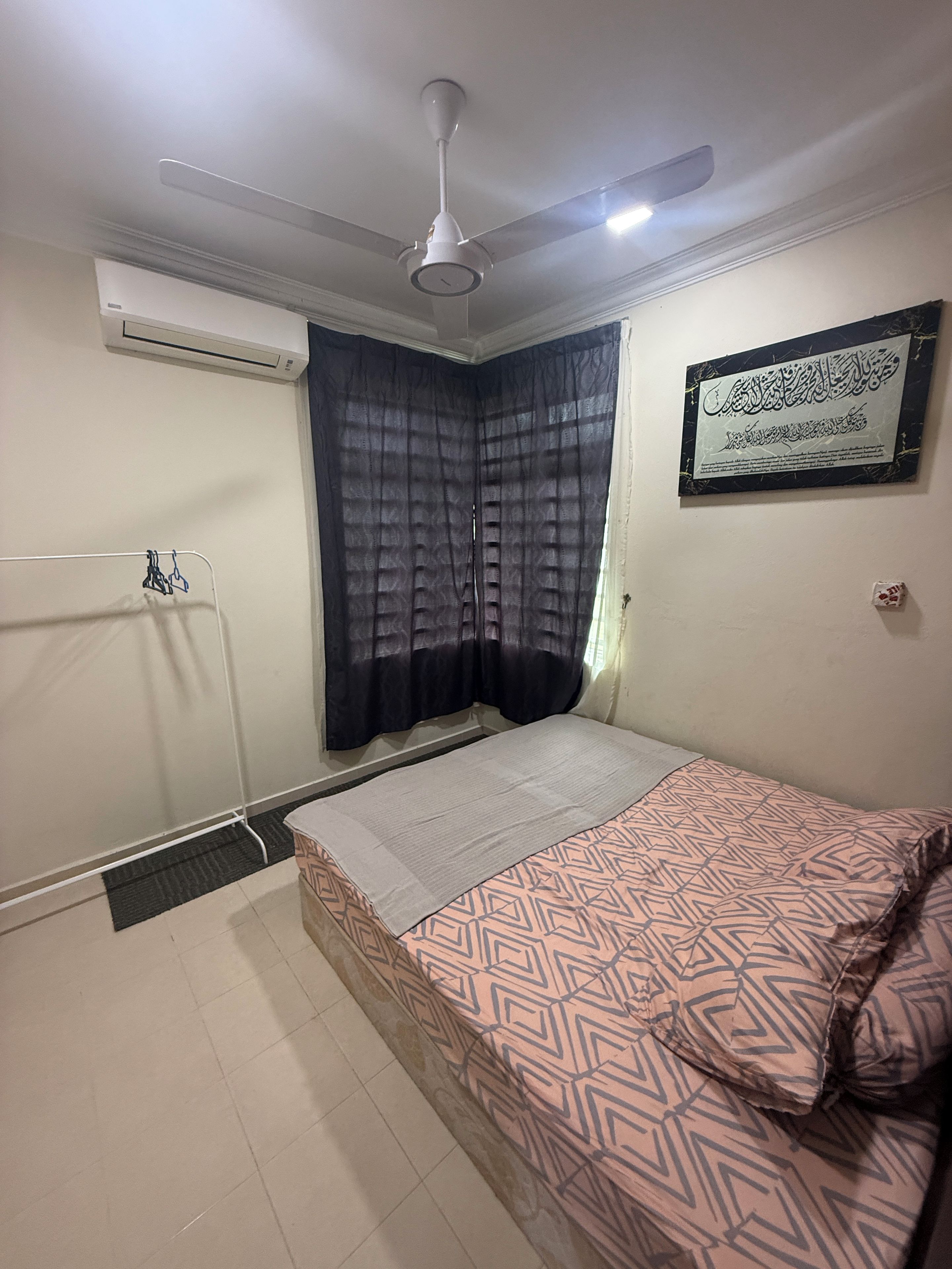 A bedroom with a bed, a ceiling fan, an air conditioning unit, a window with curtains, and a framed text on the wall.