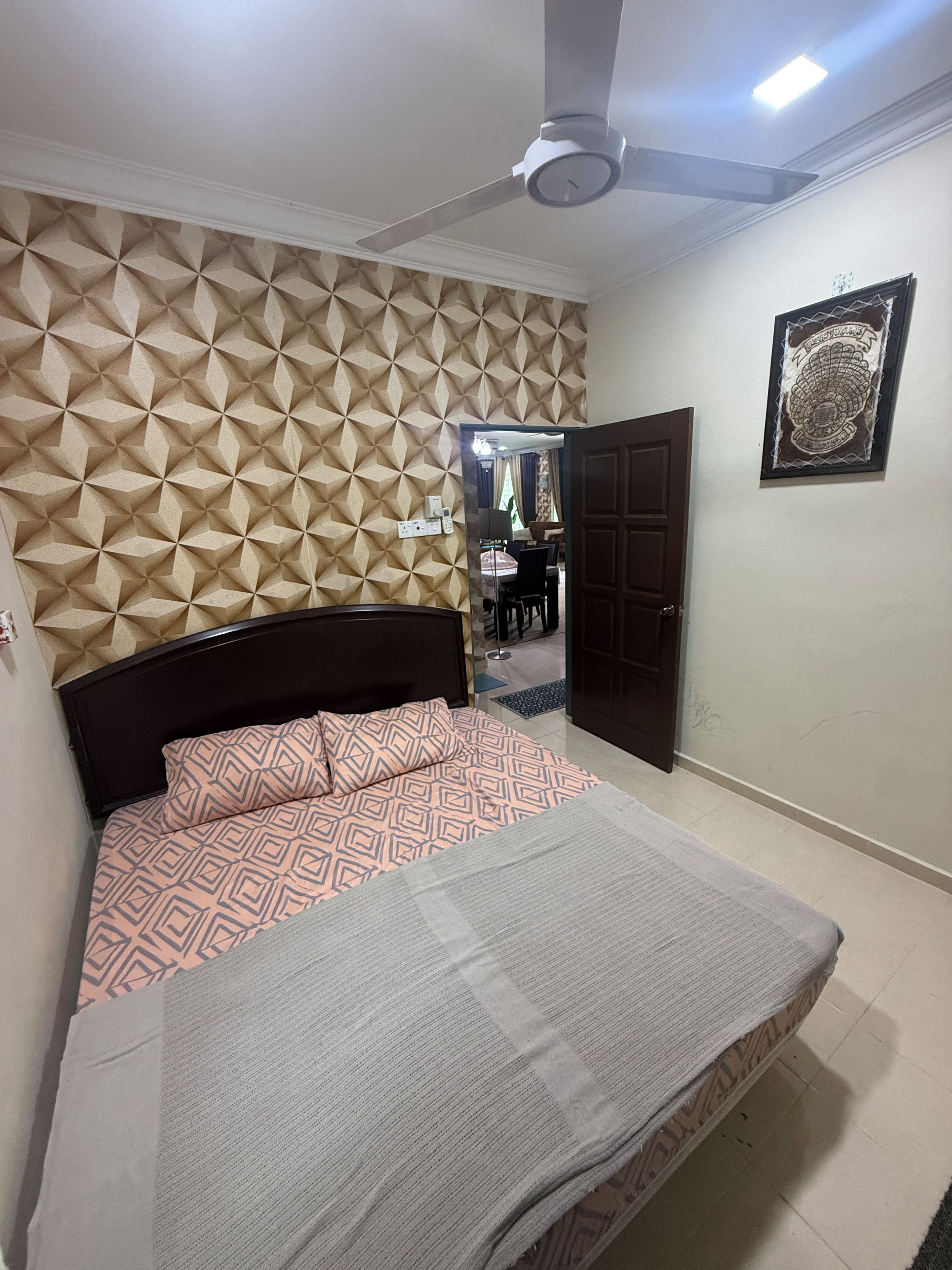 Un dormitorio con un cabecero estampado, una cama con colcha estampada, un ventilador de techo y una puerta que da a otra habitación.
