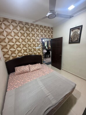 A bedroom with a patterned headboard, a bed with a patterned bedspread, a ceiling fan, and a door leading to another room. - RizQin Homestay Bachok (Bachok)