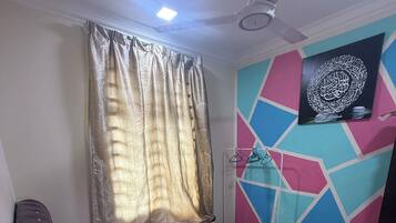 A bedroom with a bed, curtains, a ceiling fan, and a wall-mounted TV.