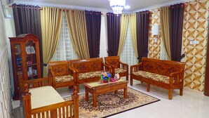 Sala de estar com móveis de madeira, um candelabro e cortinas estampadas.