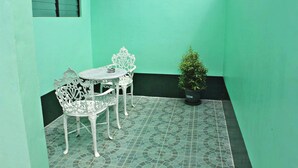 A small outdoor patio with a green wall, a white metal table and chairs, and a potted plant. - Bulalo Mangrove Inn (Calapan)
