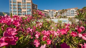 Un hôtel doté de nombreux balcons, d’une piscine et, au premier plan, d’une abondance de fleurs roses.