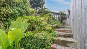 Una escalera de madera que sube hacia una casa tradicional japonesa rodeada de exuberante vegetación.
